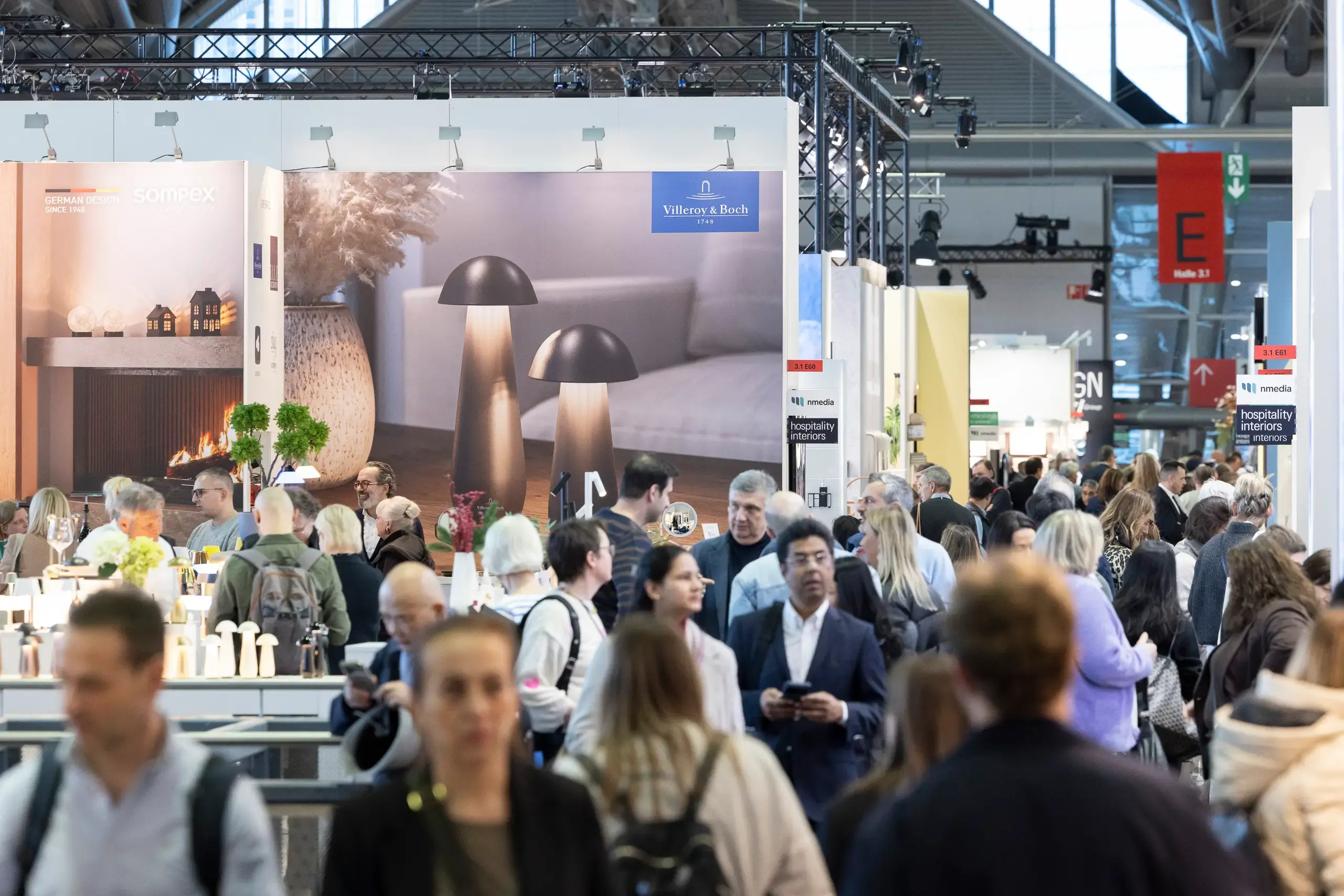 Návštěvníci procházejí halou interiérového veletrhu Ambiente Frankfurt s expozicemi značek Sompex a Villeroy & Boch, které představují designové stolní lampy a bytové doplňky